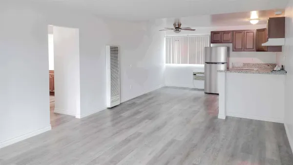a view of kitchen and empty room with wooden floor
