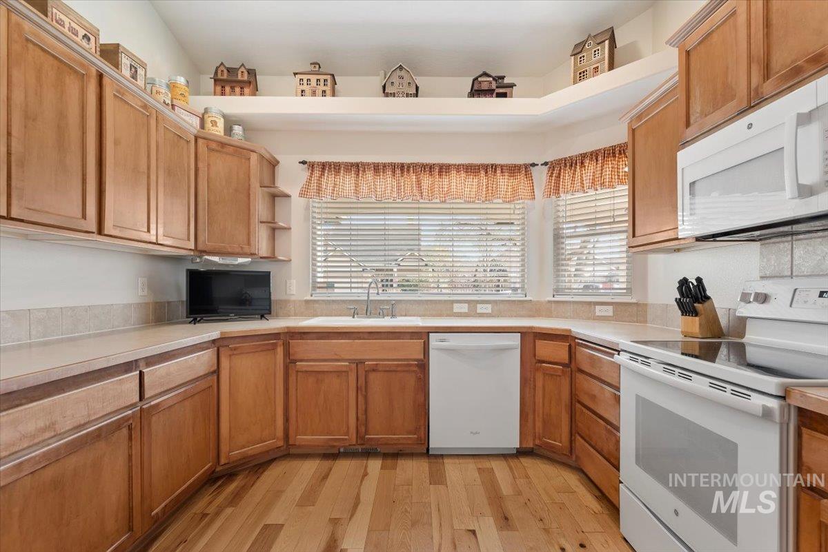 4167 North Arches Way Meridian, ID 83646 - Photo 12 of 36 Kitchen featuring white appliances, light countertops, light wood-type flooring, open shelves, and brown cabinets