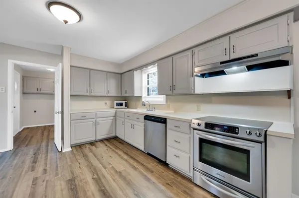 a kitchen with granite countertop wooden floors stainless steel appliances and white cabinets