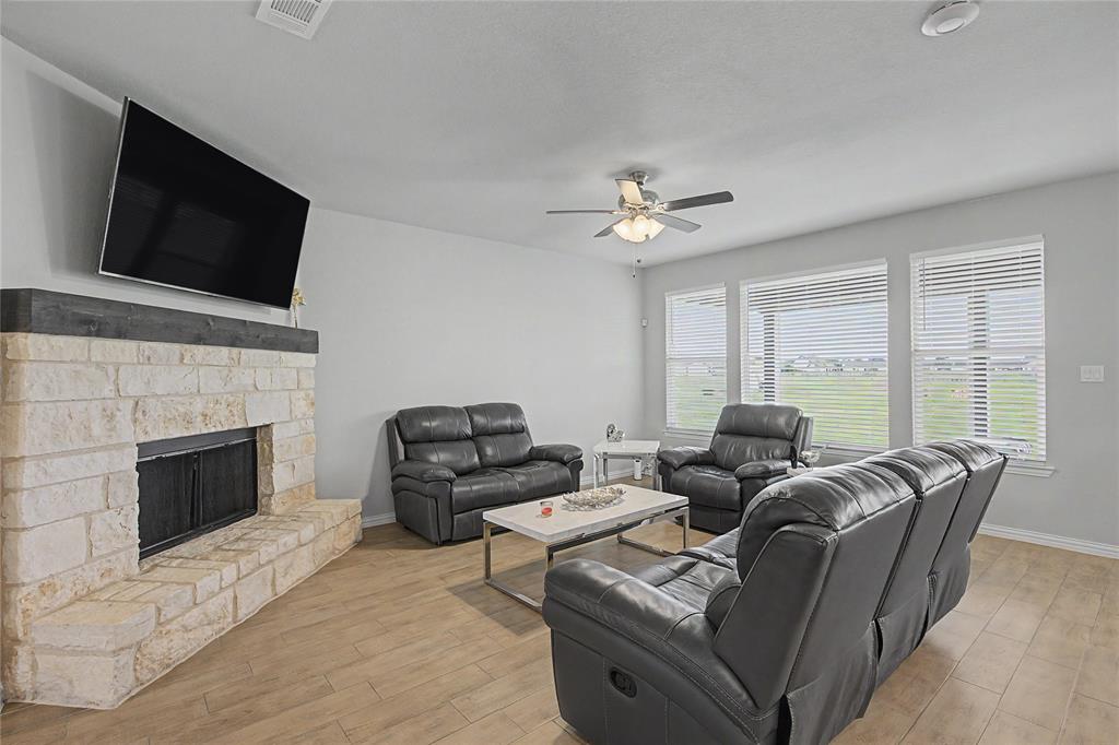 185 Chester Road Springtown, TX 76082 - Photo 13 of 40 Living area featuring a stone-faced fireplace with a dark wood-finish mantel, wood-finish flooring, and multiple windows with blinds
