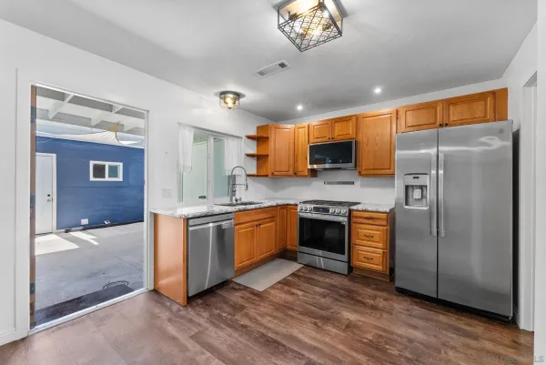 a kitchen with stainless steel appliances granite countertop a refrigerator a sink dishwasher a stove with wooden cabinets and floor