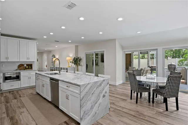 a living room with stainless steel appliances furniture wooden floor and a kitchen view