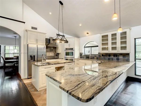 a kitchen with stainless steel appliances granite countertop a stove a sink dishwasher a refrigerator and white cabinets with wooden floor