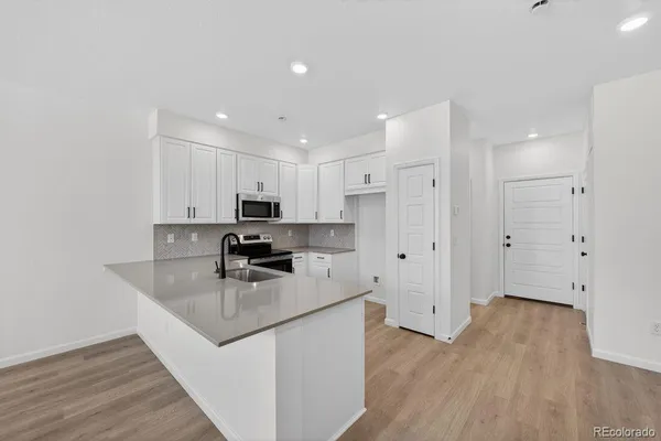 a kitchen with stainless steel appliances granite countertop a refrigerator a sink a stove and white cabinets with wooden floor