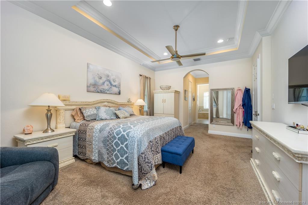 6863 Southeast Pierre Circle Stuart, FL 34997 - Photo 21 of 39 a spacious bedroom with a bed a couch and a flat tv screen on dresser