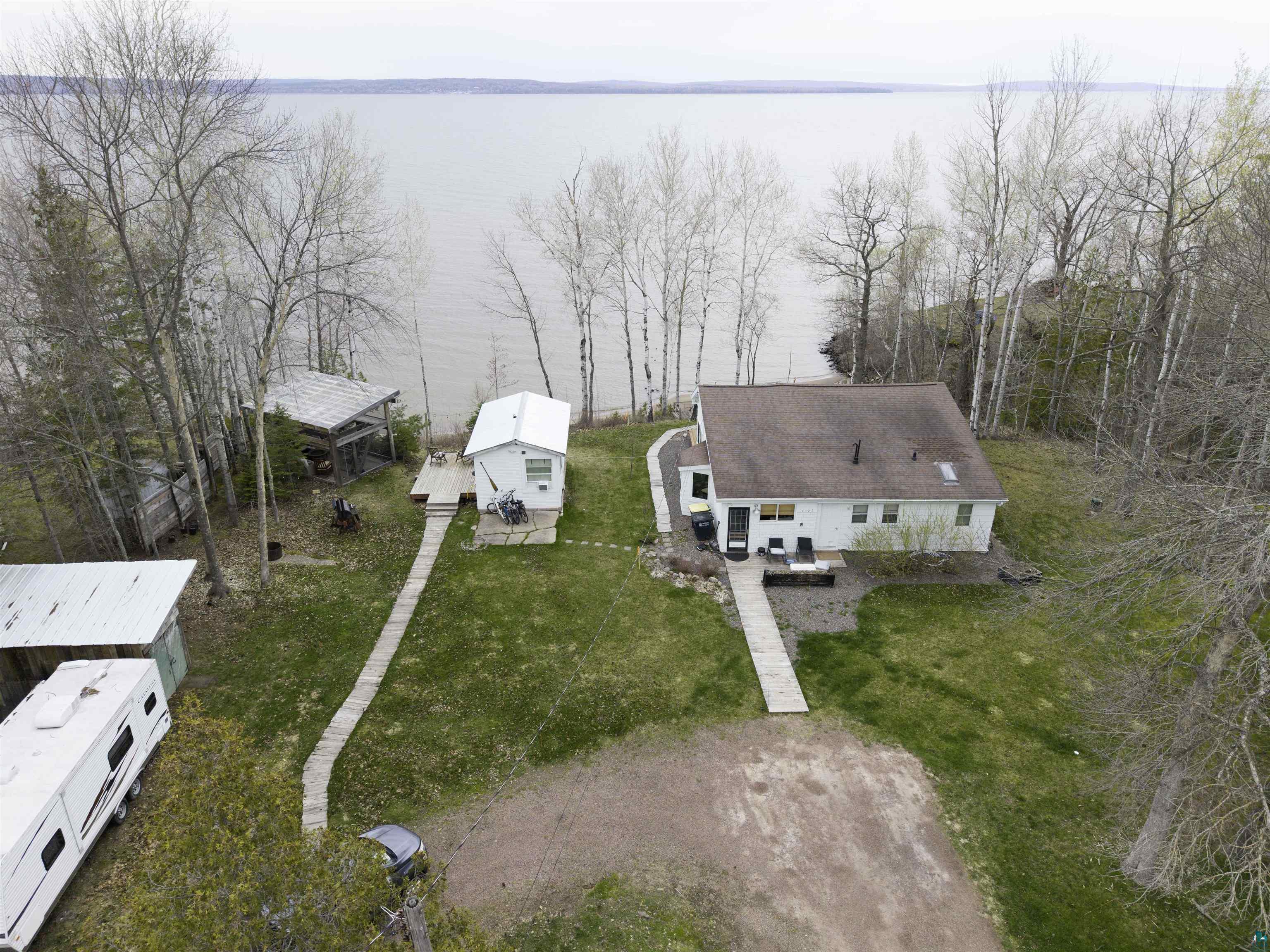 4107 B Lake Park Road Ashland, WI 54806 - Photo 2 of 23 Waterfront property featuring a primary residence, a detached secondary structure with a deck, a separate outbuilding, and mature trees