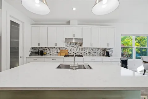 a kitchen with stainless steel appliances a stove a sink a oven a dining table and chairs with wooden floor