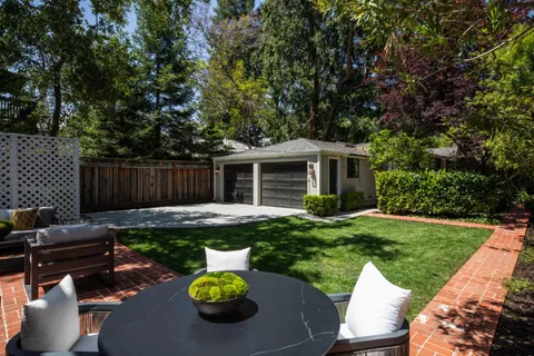 a view of a backyard with table and chairs potted plants and a large tree