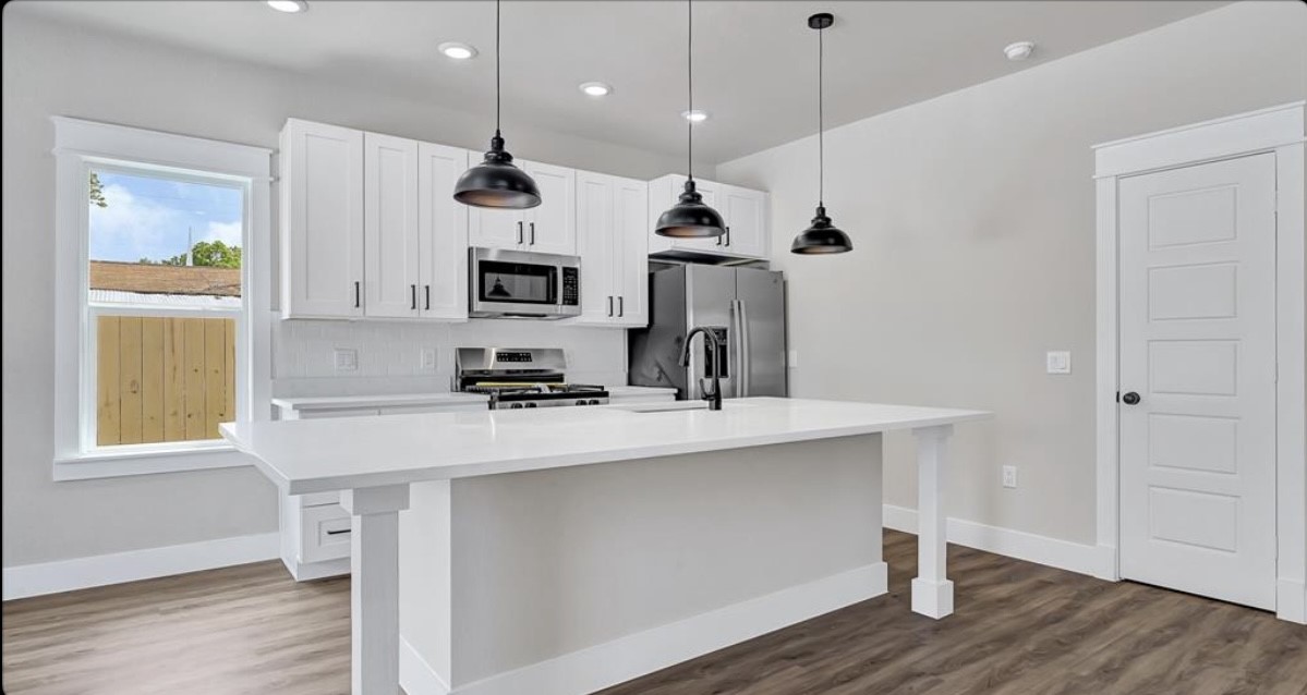 204 Booker T Washington Street, Unit B Conroe, TX 77301 - Photo 3 of 13 a kitchen with kitchen island a sink stainless steel appliances and wooden floor