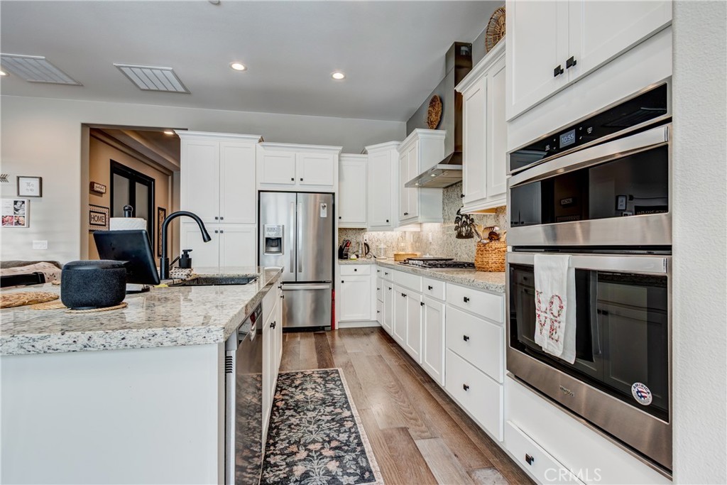 11137 Briar Rose Court Corona, CA 92883 - Photo 22 of 75 a kitchen with stainless steel appliances kitchen island granite countertop a stove top oven a sink a refrigerator and white cabinets