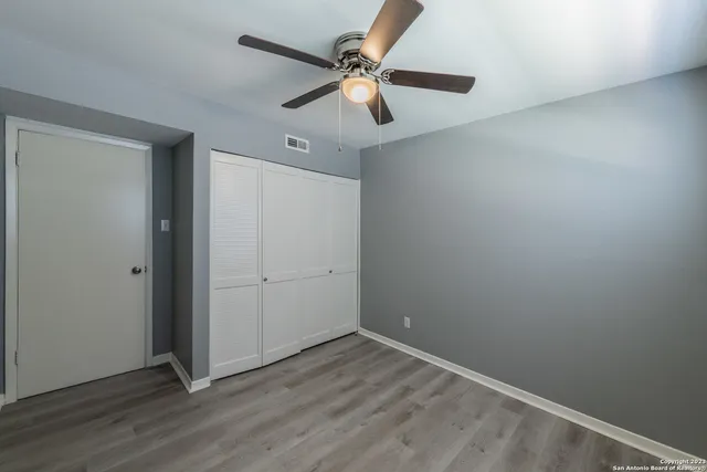 an empty room with wooden floor fan and windows