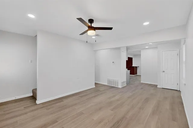 a view of an empty room with wooden floor and a ceiling fan
