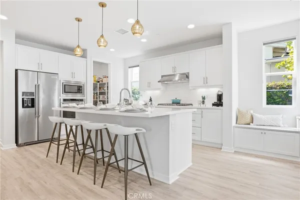 a kitchen with stainless steel appliances kitchen island granite countertop a refrigerator a stove a sink dishwasher and white cabinets with wooden floor