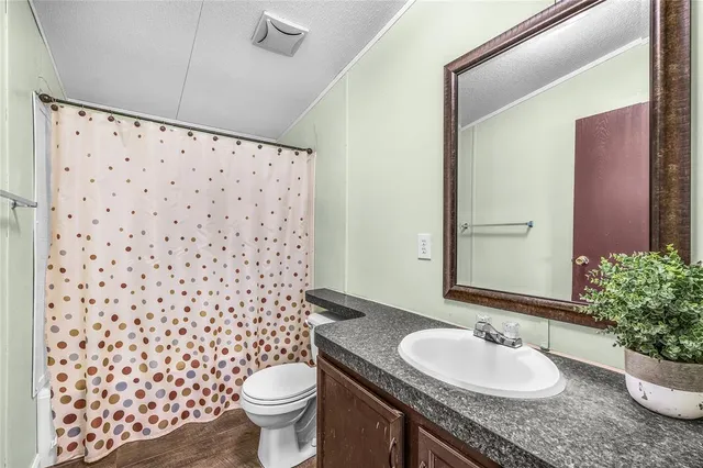 a bathroom with a granite countertop toilet a sink a mirror a shower curtain