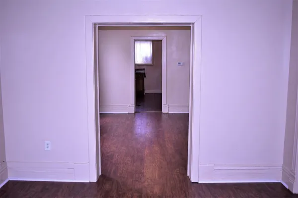 a view of a hallway with wooden floor and a small refrigerator