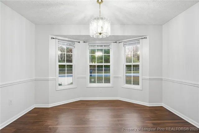 an empty room with wooden floor chandelier and windows