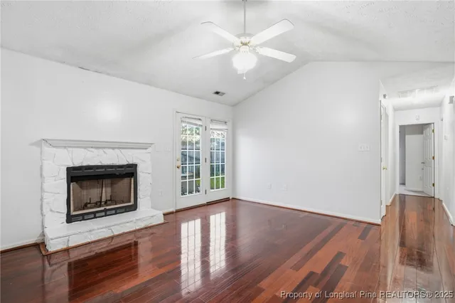 an empty room with wooden floor a chandelier fan a fireplace and windows