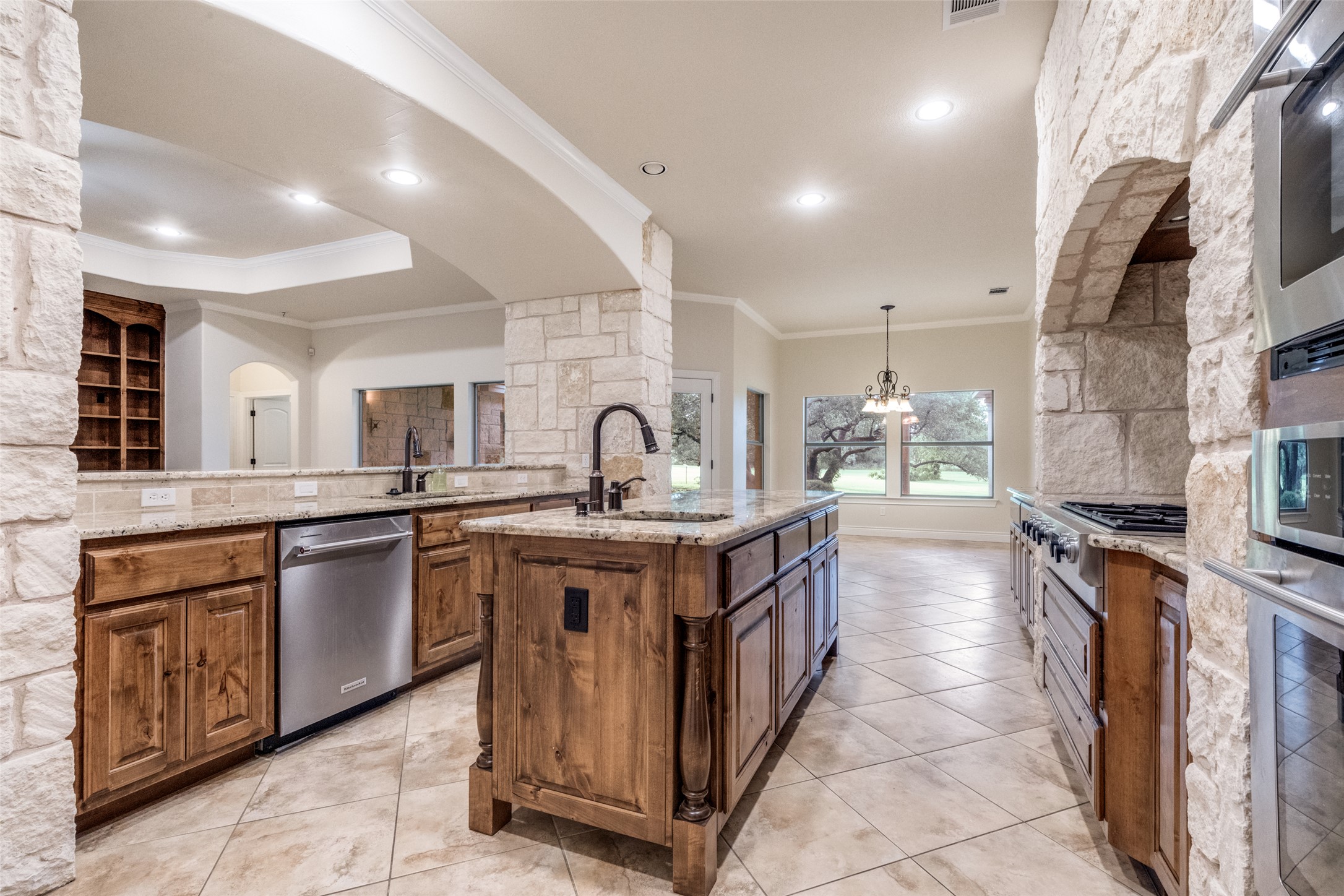 101 Copper Leaf Court Georgetown, TX 78633 - Photo 11 of 31 Open-concept kitchen featuring stone columns, wood-finish cabinetry, stainless steel appliances, and a central island with a sink