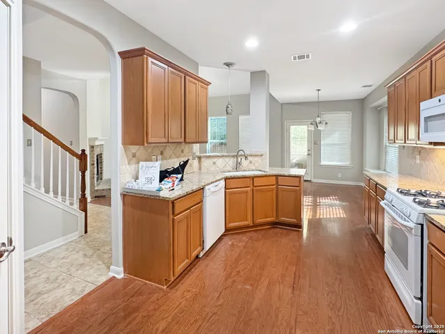 a kitchen with stainless steel appliances granite countertop a stove top oven a sink a refrigerator white cabinets and wooden floor