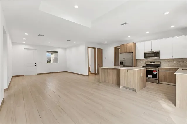 a view of kitchen with stainless steel appliances kitchen island granite countertop a stove a sink a refrigerator and white cabinets with wooden floor