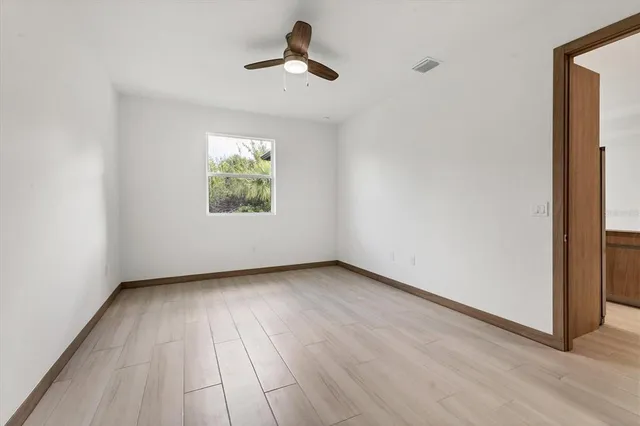 an empty room with wooden floor chandelier fan and windows