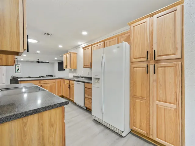 a kitchen with stainless steel appliances granite countertop a refrigerator a sink and white cabinets with wooden floor