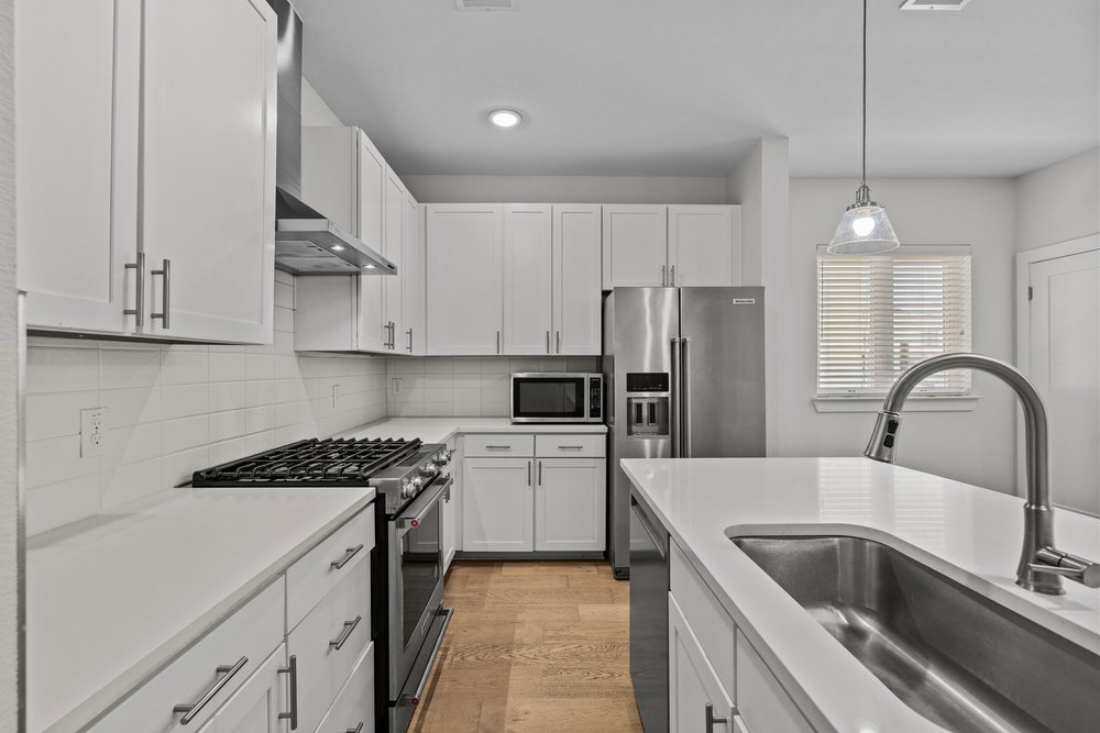 2827 Manor Road, Unit 2201 Austin, TX 78722 - Photo 15 of 40 Modern kitchen featuring white shaker cabinetry, stainless steel appliances, light-toned countertops, and wood-finish flooring