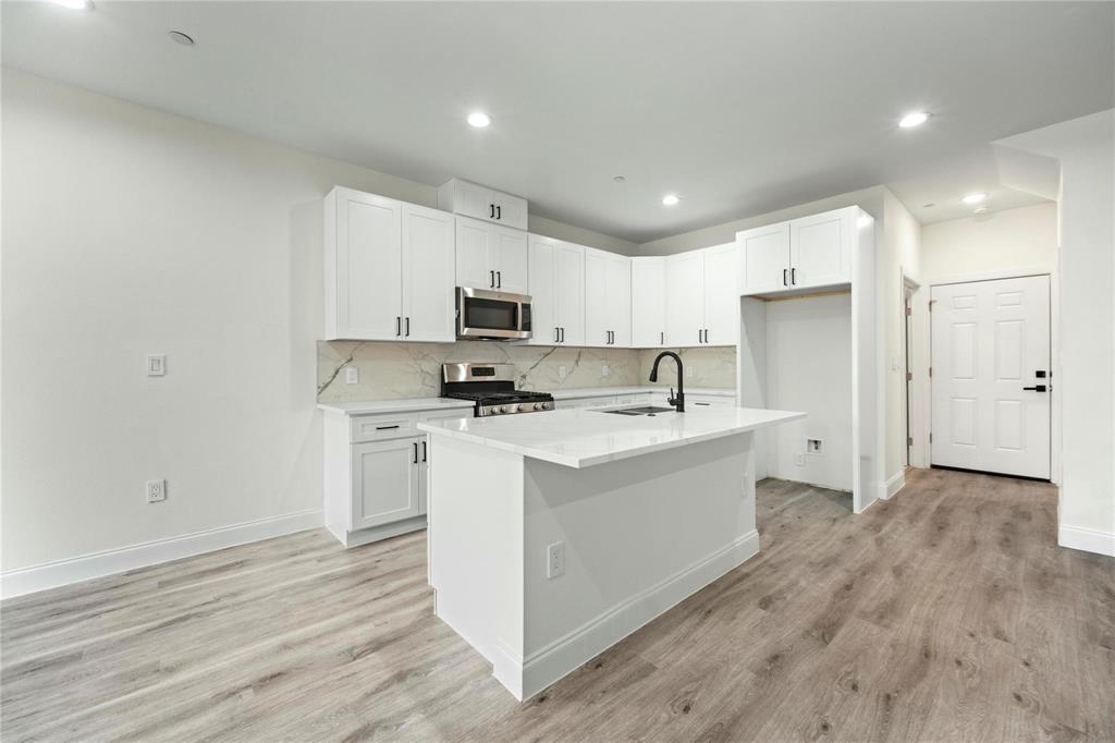 6238 Dewitt Street Sachse, TX 75048 - Photo 4 of 21 a kitchen with kitchen island a sink a stove a microwave and white cabinets