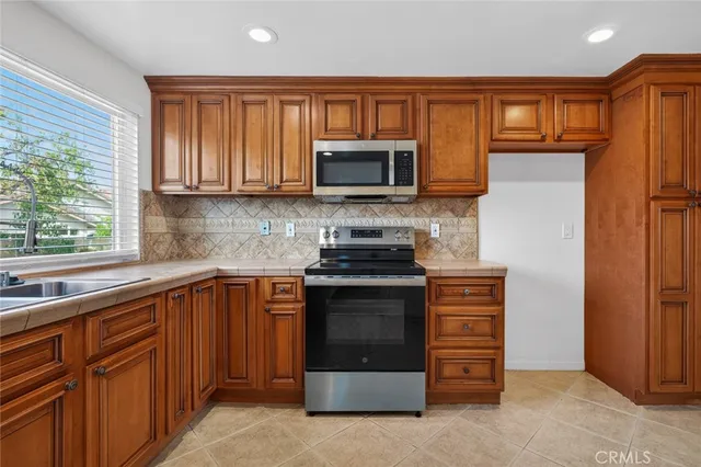 a kitchen with stainless steel appliances granite countertop a stove top oven a refrigerator and a sink with wooden cabinets