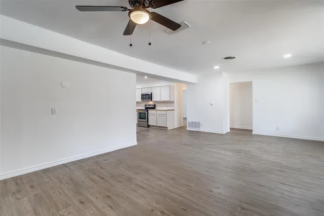 an empty room with wooden floor fan and windows