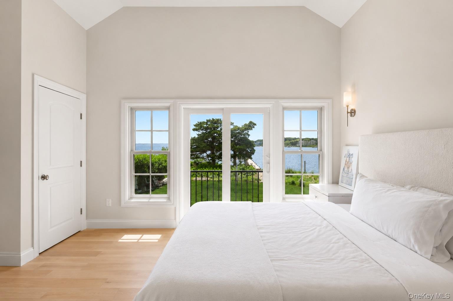 65 Shore Road Westhampton, NY 11977 - Photo 14 of 24 Vaulted ceiling bedroom featuring wood-finish flooring, a wall sconce, and a balcony with wrought iron railing overlooking a body of water