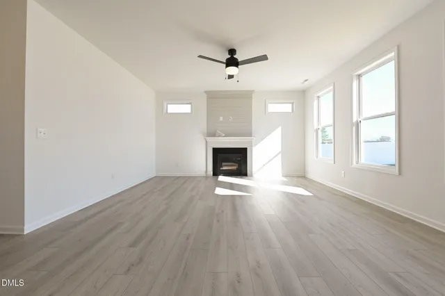 a view of a livingroom with a fireplace a ceiling fan and wooden floor