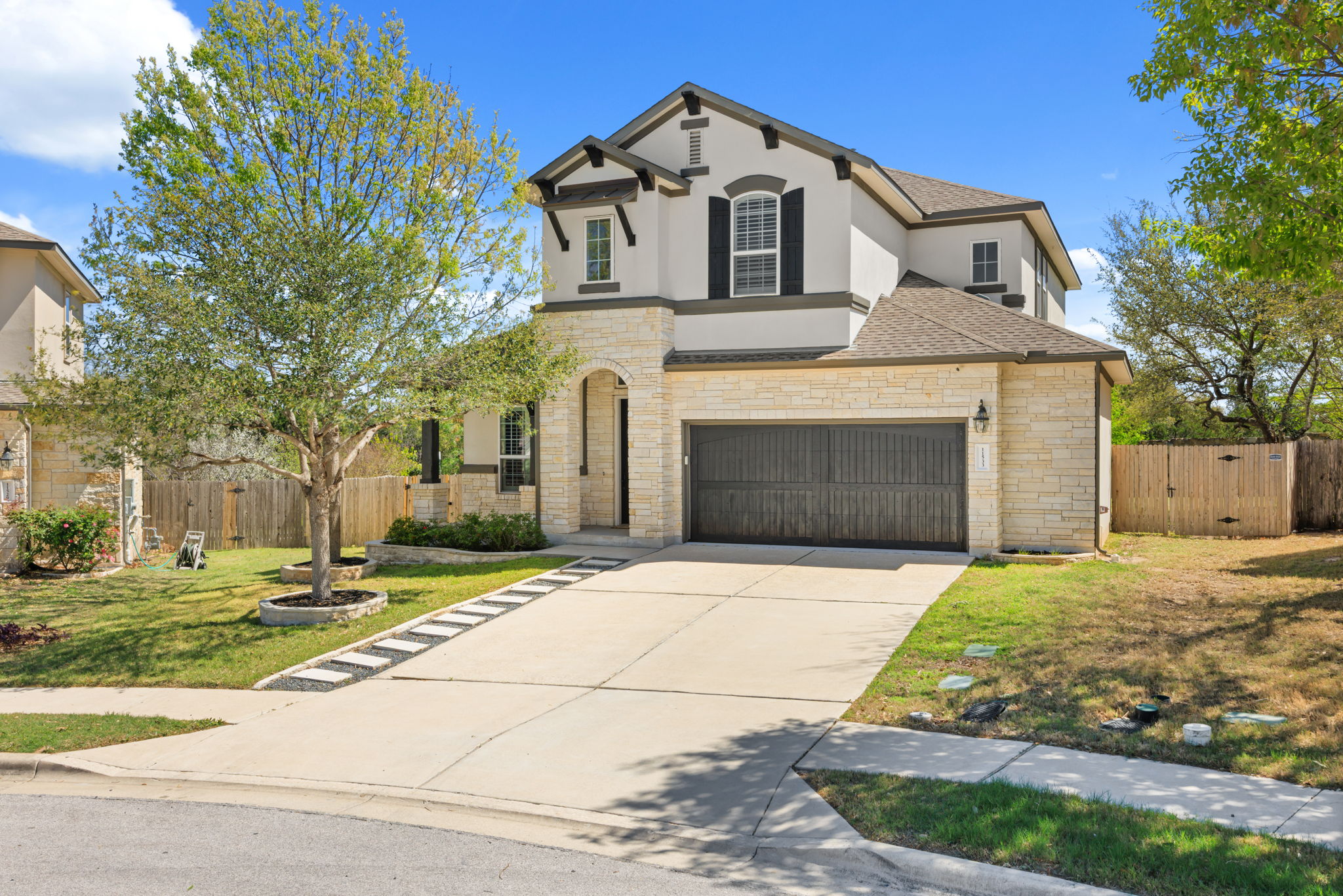 View of front of home with a gate, concrete driveway, stucco siding, stone siding, and a shingled roof