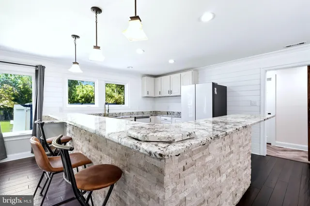 a kitchen with stainless steel appliances granite countertop a stove a sink a refrigerator a dining table and chairs with wooden floor