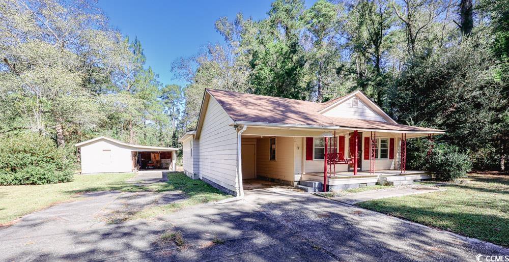 View of front facade featuring driveway, an outbuilding, covered porch, and an attached carport