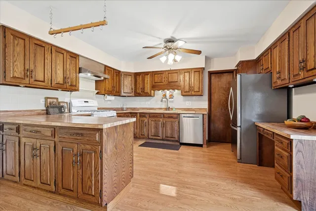 a kitchen with stainless steel appliances granite countertop a refrigerator a sink dishwasher a stove with wooden cabinets and floor