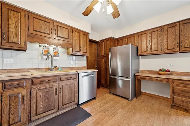 a kitchen with stainless steel appliances granite countertop a refrigerator a sink dishwasher a dining table and chairs with wooden floor