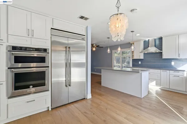 a kitchen with stainless steel appliances granite countertop a refrigerator a oven and white cabinets with wooden floor