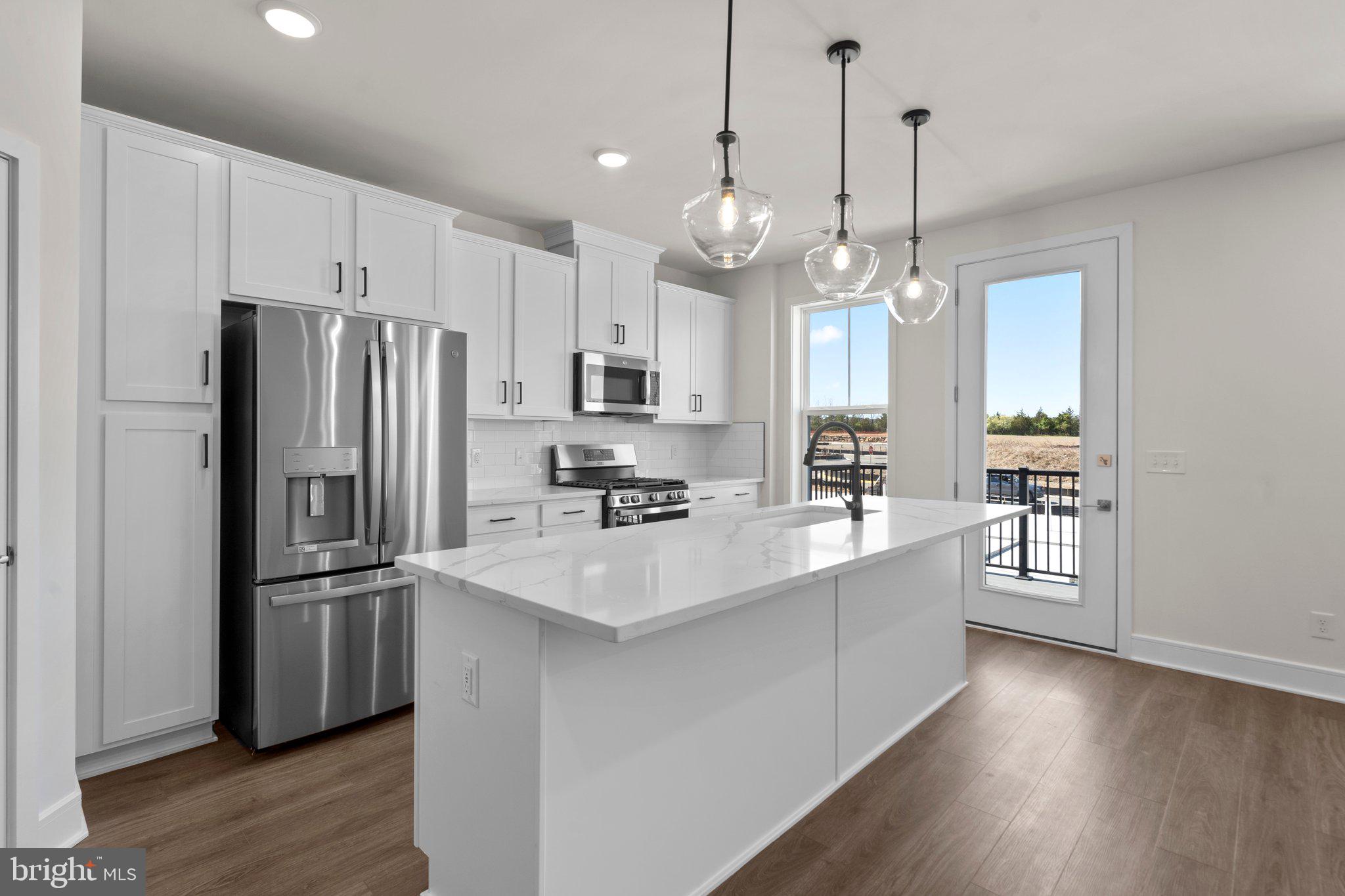 a kitchen with stainless steel appliances a refrigerator a sink cabinets wooden floor and a chandelier