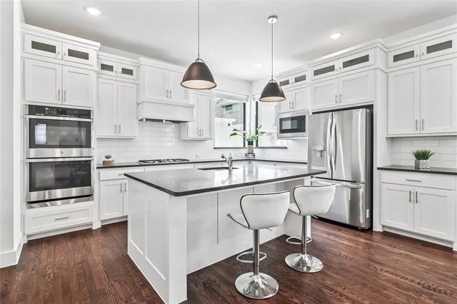 a kitchen with stainless steel appliances granite countertop a stove a sink and white cabinets with wooden floor