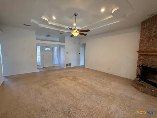 a view of an empty room with chandelier fan and fire place