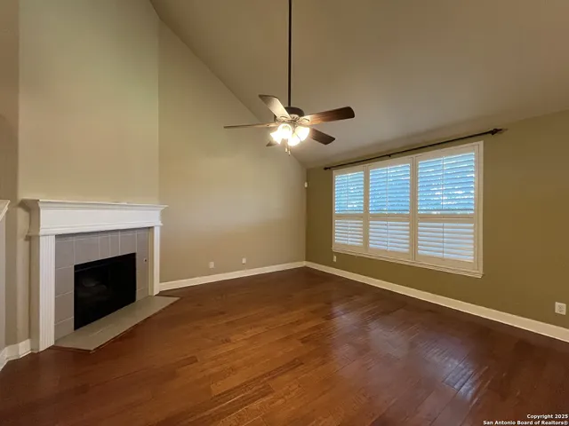a view of an empty room with wooden floor fireplace and a window