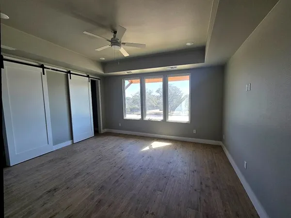 an empty room with wooden floor fan and windows