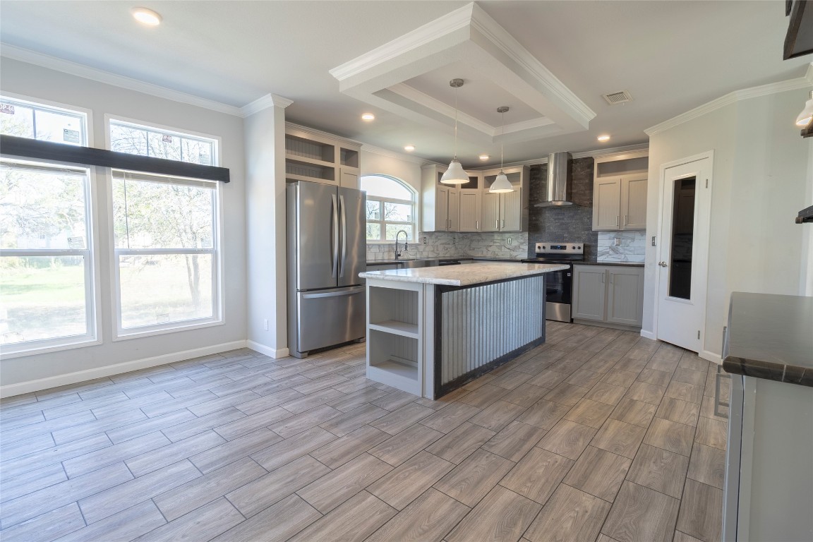425 High View Ranch Drive Cedar Creek, TX 78612 - Photo 30 of 36 Kitchen featuring open shelves, gray cabinets, appliances with stainless steel finishes, wall chimney range hood, and hanging light fixtures