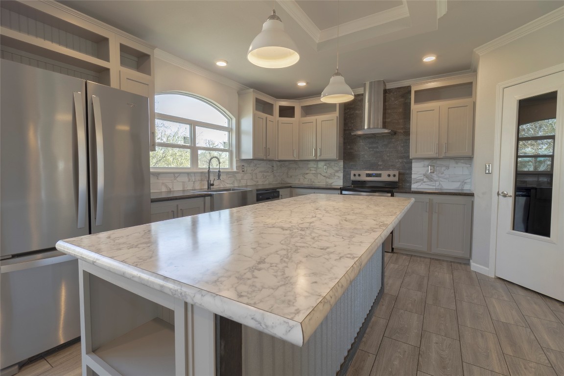 425 High View Ranch Drive Cedar Creek, TX 78612 - Photo 31 of 36 Kitchen featuring stainless steel appliances, light countertops, a kitchen island, hanging light fixtures, and wall chimney range hood