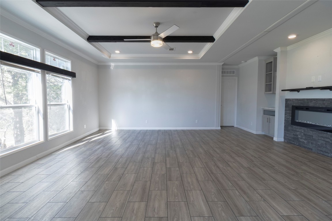 425 High View Ranch Drive Cedar Creek, TX 78612 - Photo 35 of 36 Unfurnished living room featuring wood tiled floors, ceiling fan, a glass covered fireplace, recessed lighting, and crown molding