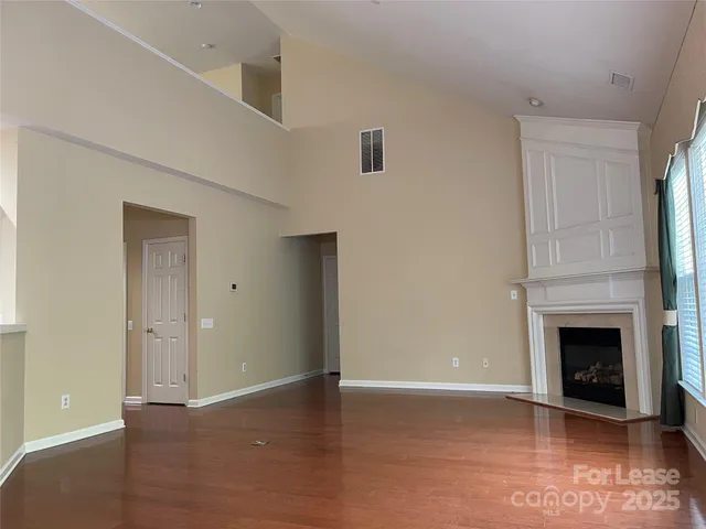 a view of an empty room with wooden floor fireplace and a window