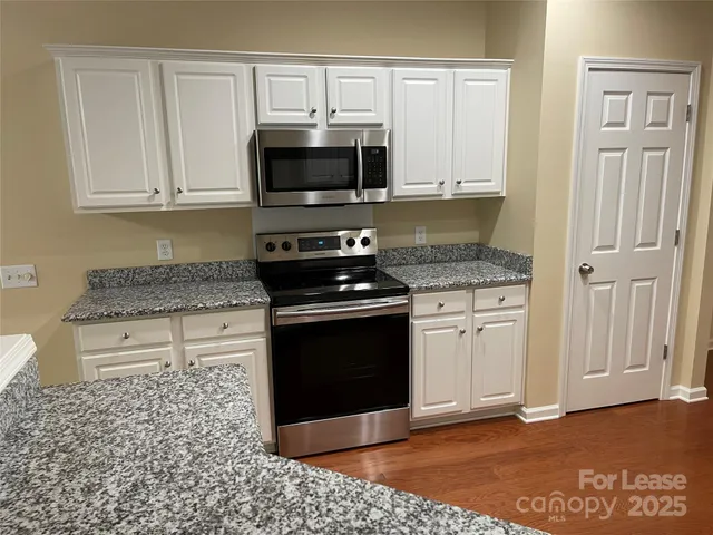 a kitchen with granite countertop white cabinets stainless steel appliances and a counter space
