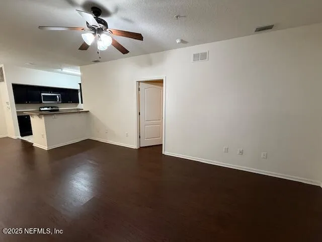 an empty room with wooden floor a ceiling fan and a kitchen view
