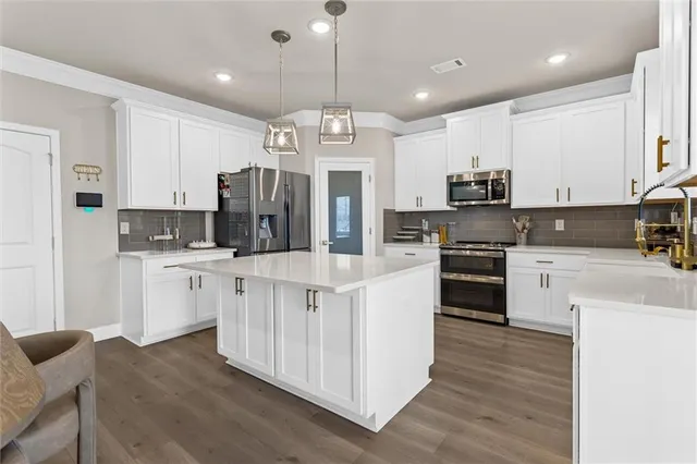 a large kitchen with stainless steel appliances kitchen island granite countertop a stove a sink a refrigerator and white cabinets with wooden floor